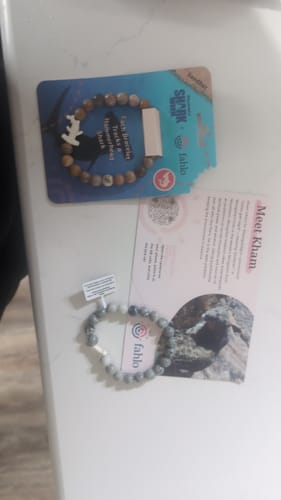 Customer's gray Ascent Bracelet next to its product packaging and informational card on a flat surface.