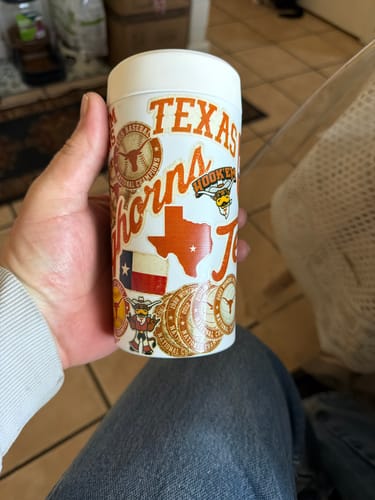 Customer's white Universal Buddy can cooler covered in Texas Longhorns stickers being held in a person's hand.