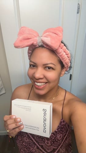 Customer holding the Seranova Microneedling Infusion System box while wearing a plush pink bow headband.