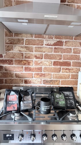 Customer's Recce Party coffee bundle, including four coffee bags and a black mug, on a kitchen stove.