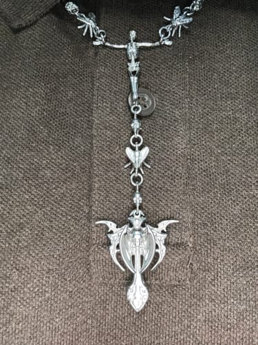 Customer's Rotten Rosary silver-toned chain featuring intricate figure and wing detailing against a brown textured shirt.
