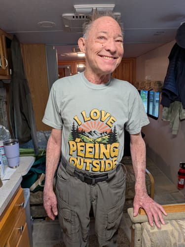 Reviewer smiling while wearing the light green I Love Peeing Outside T-shirt in a camper setting.