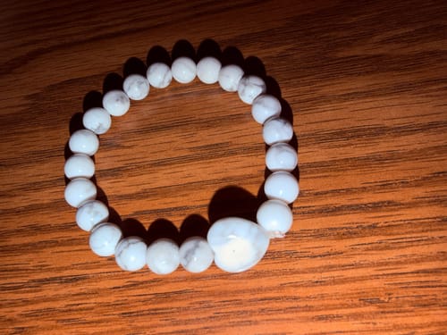 Customer's Howlite bracelet from the VIP Crystal Club, made of smooth white marble-like stones on a wooden surface.