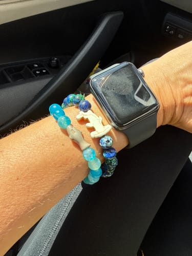 Customer's wrist wearing two blue-beaded Voyage Bracelets with shark charms and a smartwatch.