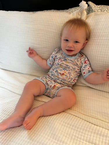 Customer's child wearing Birthday Boy Short Pajamas with a birthday print, sitting on a white bed.