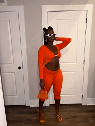Customer's orange Naked Cutout Capri Jumpsuit with matching handbag and heels in a home setting.