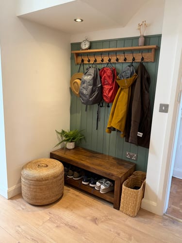 Customer's Solid Oak Walnut Coat Rack with Shelf mounted on a green wall, holding coats, hats, and backpacks.