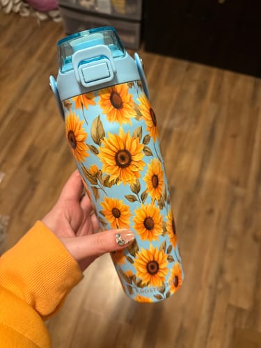 Customer's Bottle Buddy 24oz in sunflower print with a blue lid, held in a hand.