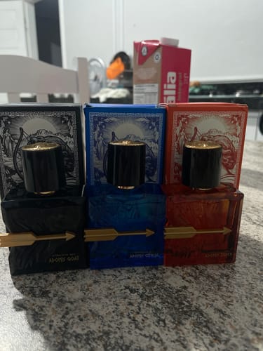 Reviewer's three Kit Adonis perfume bottles in black, blue, and red with matching boxes on a counter.