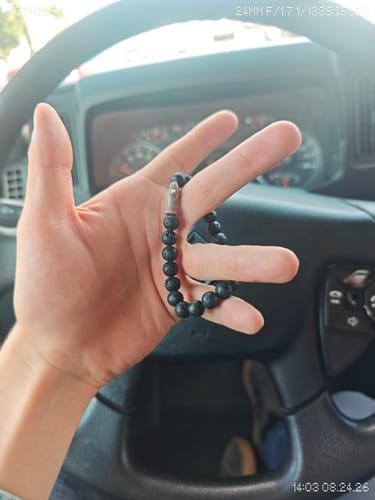 Customer's black lava Voyage Bracelet held in hand inside a car.
