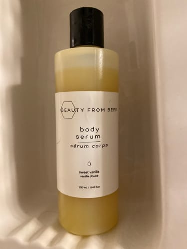 Customer's Beauty From Bees Body Serum in Sweet Vanilla fragrance, sitting in a shower niche.