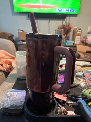 Customer's shiny cinnamon Thicc Buddy 40oz mug with straw sitting on a cluttered surface.