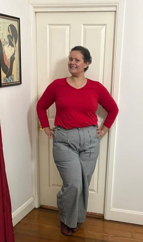 Customer's Construction Pants in pinstripe fabric worn with a red top, posing at home.
