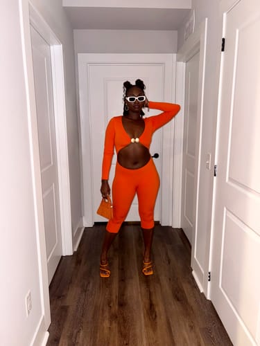 Reviewer's orange Naked Cutout Capri Jumpsuit with gold hardware, styled with white sunglasses.