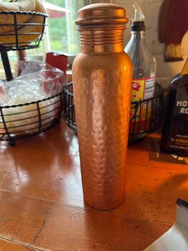 Customer's hand-hammered copper Certified Ayurveda water bottle standing on a kitchen counter.
