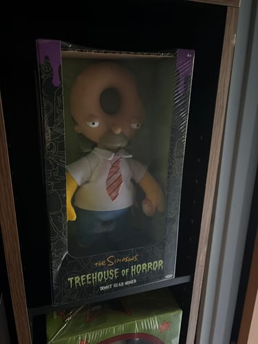 Customer's Donut Head Homer Treehouse of Horrors plush figure inside its decorative box on a shelf.