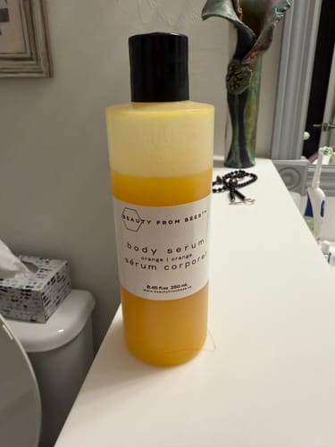 Customer's orange Beauty From Bees Body Serum bottle sitting on a bathroom vanity.