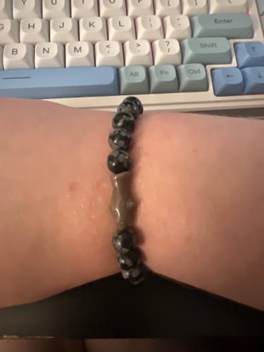 Customer's wrist wearing a dark, beaded Voyage Bracelet with a shark-shaped charm, shown in front of a keyboard.
