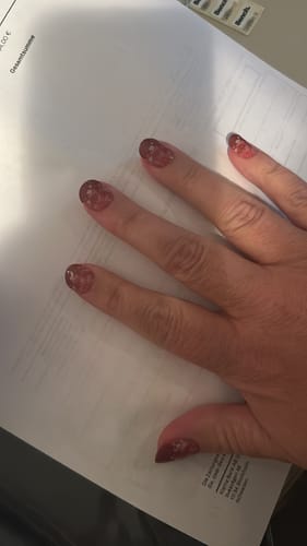 Kundenhand mit aufgetragenen Dipped In Blooms UV Gel Nail Wraps, die ein florales Muster auf rotem Untergrund zeigen.