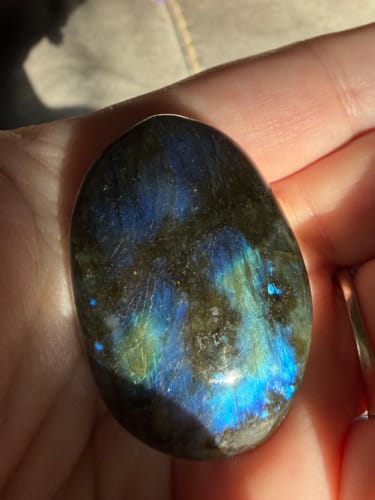 Reviewer's hand holding a smooth, oval crystal showing vibrant blue and green light flashes.