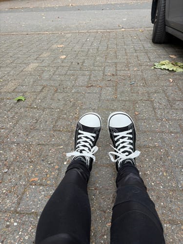 Kunde trägt die schwarz-weißen Roam I Barfußschuhe auf einem gepflasterten Gehweg.
