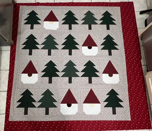 Customer's Gnomes Gone Wild in Greige Quilt Kit, a pieced quilt with pine trees and gnomes, laid over red fabric.