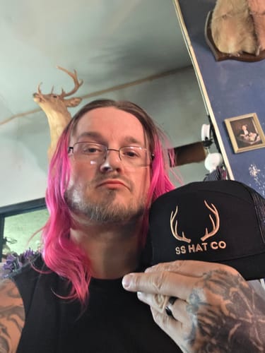 Customer's Hat of the Month Crew cap with antlers logo, held up by reviewer with tattoos