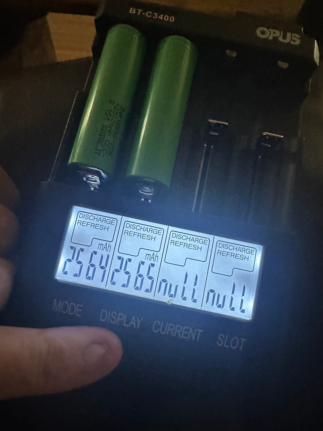 Two green INR18650-25R cells in an Opus BT-C3400 charger, its screen showing 2564 and 2565 mAh