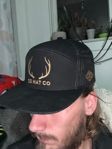 Customer's Hat of the Month Crew black trucker hat with gold deer antler logo, worn by a person.