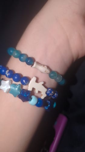 Customer's hand wearing three stacked Voyage Bracelets with blue beads, star shapes, and shark charms.