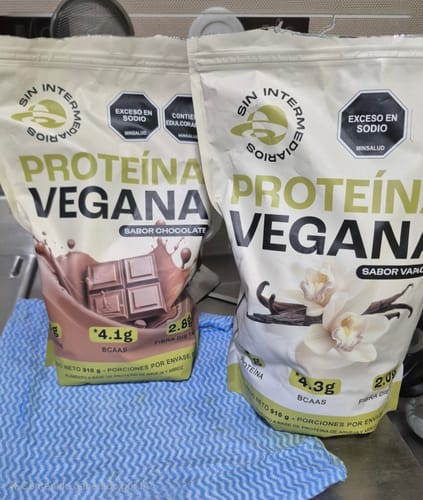 Reviewer's two bags of Proteína Vegana in chocolate and vanilla flavors, resting on a blue patterned cloth.