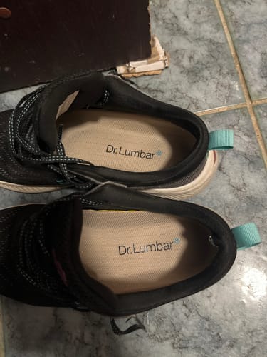 Customer's pair of black Dr. Lumbar athletic shoes viewed from above, resting on a tiled floor.