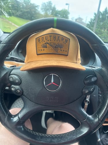 Customer's Hat of the Month Crew cap with gold patch, resting on a steering wheel inside a car.