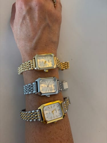 Customer's hand showing three Claire De Mains watches with different metal finishes stacked on their wrist.