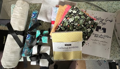 Customer's Mystery Grab Bag fabric bundles tied with ribbon, alongside product flyer on a work surface.