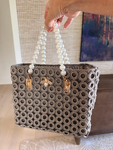 Customer's completed Pearl Bee Crochet Bag held by hand, featuring gray circular pattern and pearl handle.