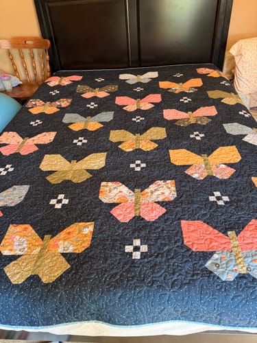 Customer's completed Missing Pieces quilt with colorful butterfly patterns spread on a dark bed frame.