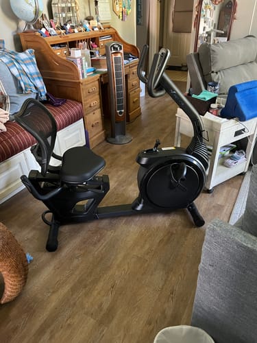 Reviewer's black recumbent exercise bike fully assembled and positioned on a wooden floor in a home office.