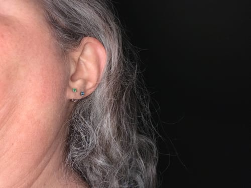 Customer's Comfort Earrings Bundle on an earlobe, showing two small, delicate studs.