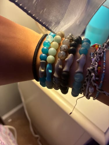 Customer's wrist wearing multiple Voyage Bracelet shark-themed beaded bracelets in blue, black, and grey tones.