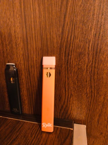Customer's orange Rollz THCA vape standing upright next to a black vape on a wooden surface.