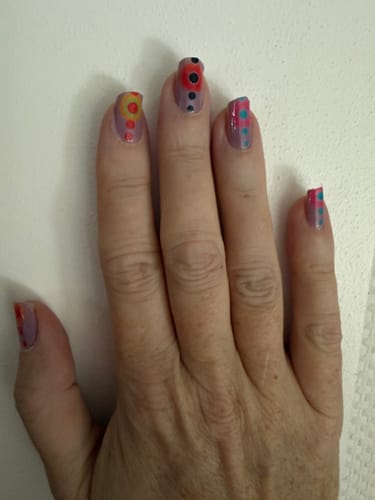 Customer's hand showcasing Less Is More nail wraps with colorful polka dot patterns on each fingernail.