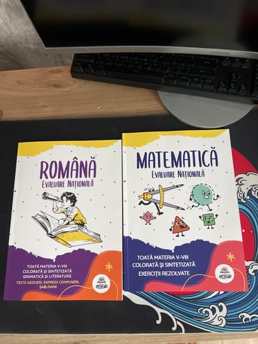 Customer's Pachet Evaluare Națională culegeri de Română și Matematică pe un mousepad, cu coperti colorate ilustrate.