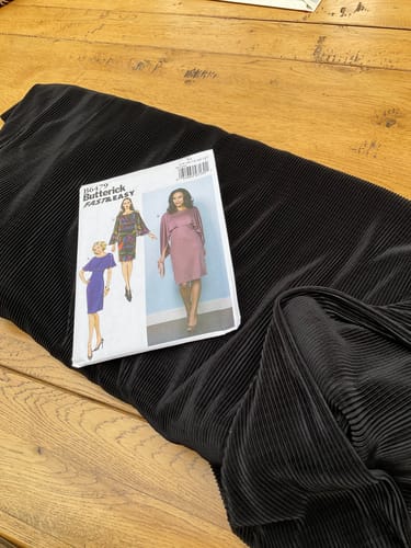 Reviewer's black linear textured polyester fabric laid out on a wooden table with a sewing pattern envelope.