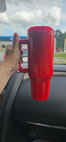 Customer's hand holding a red Cherry Glaze Thicc Buddy mug in a car