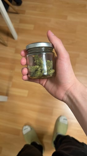 Customer's hand holding a small glass jar filled with green, dense buds of CALI MIX AAA+ flower.