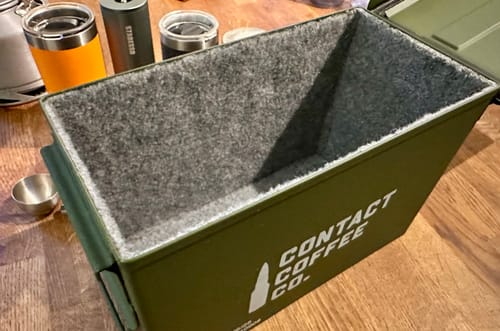Customer's green M2A1 Ammo Tin, lined with gray felt, resting on a wooden table.