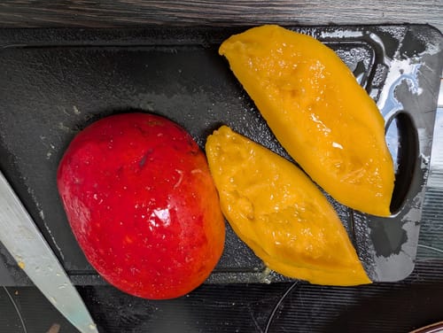 Customer's Zill Mango sliced on a black cutting board, showing bright yellow flesh and a vibrant red skin.