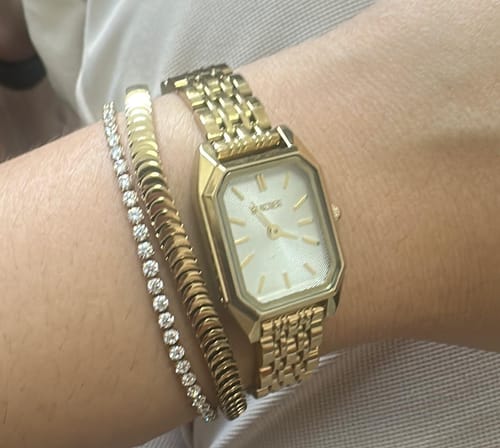 Customer's Isabell Petite Gold watch worn on a wrist alongside two gold-toned bracelets.
