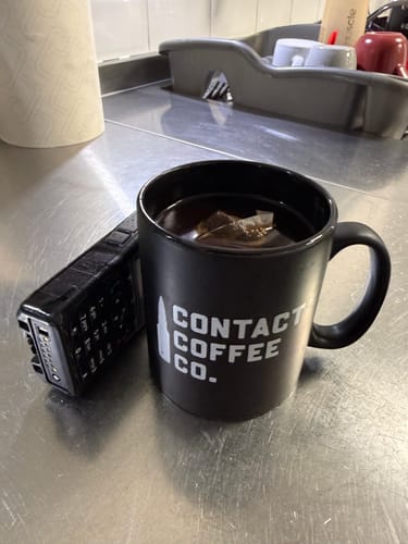 Customer's Contact Coffee Co. black mug with a coffee brew bag steeping in hot water, sitting next to a radio.